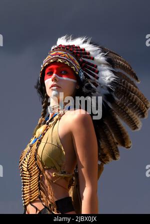 Eine indianische Ureinwohnerin steht vor grauen Regenwolken. Sie trägt einen gefiederten Kopfschmuck und trägt traditionelle indische Kleidung. Stockfoto