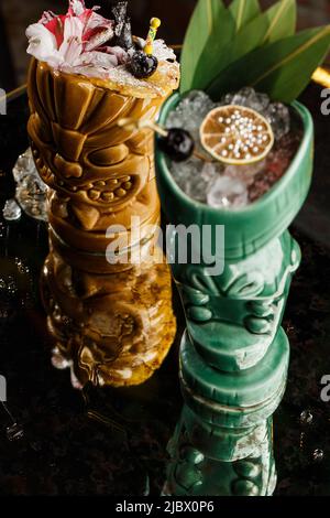 Tiki Getränke Cocktails. Zwei Cocktails in verschiedenen Gläsern vor dem Hintergrund einer Bar, die mit Trockenfrüchten und tropischen Blättern dekoriert ist Stockfoto