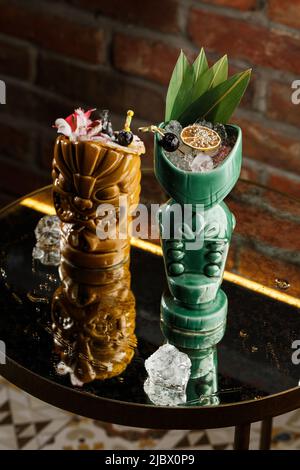 Tiki Getränke Cocktails. Zwei Cocktails in verschiedenen Gläsern vor dem Hintergrund einer Bar, die mit Trockenfrüchten und tropischen Blättern dekoriert ist Stockfoto