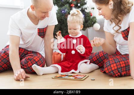 Kleinkind mit Cochlea-Implantat spielt unter dem weihnachtsbaum mit den Eltern - Taubheit und Vielfalt und innovative medizinische Technologien für das Hören Stockfoto