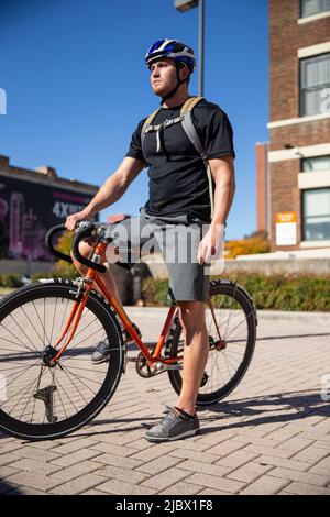 Mann, der eine Pause einnahm, während er mit dem Fahrrad zur Arbeit auf dem Single-Speed-Fahrrad unterwegs war Stockfoto