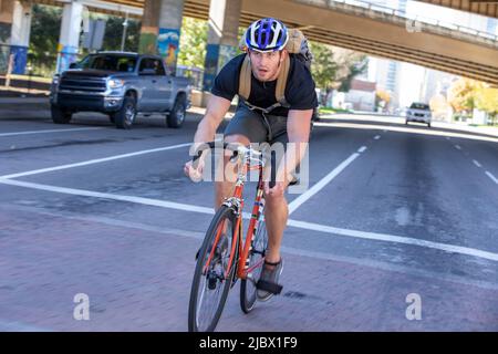 Action-Aufnahme eines Mannes, der mit dem Fahrrad unter einer Autobahnüberführung in einer belebten Stadt arbeitet Stockfoto