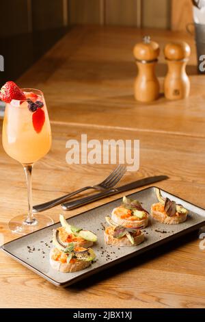 Gebackene Bruschetta mit Lachs, Käse, getrockneten Tomaten und Avocado auf grauem Teller auf hellem Hintergrund. Stockfoto