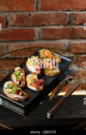 Bruschettas mit Gemüse. Beginnen Sie die Gerichte mit Kirschtomaten, Avocado, Frischkäse und Garnelen. Zusammensetzung des Essens, leckeres italienisches Essen. Stockfoto