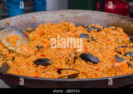 Orangenpaella mit Garnelen, Muscheln, Reis, Gewürzen, Safran in einer riesigen Paella-Pfanne Stockfoto