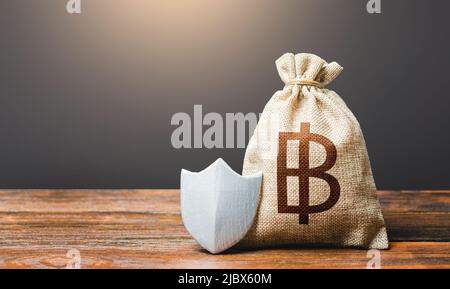 Tasche mit thai Baht Symbol und Schutzschild. Gewährleistung der Investitionssicherheit in Thailand. Verringerung der Korruptionsrisiken bei der Geschäftstätigkeit. Guar Stockfoto