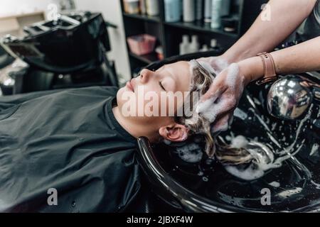 Frau, die Shampoo anwendet und die Haare des Kunden massiert. Eine Frau, die sich beim Friseur die Haare wäscht. Hochwertige Fotos Stockfoto