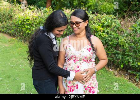 Eine Tochter hält die Hände ihrer Mutter auf ihren schwanger werdenden Bauch. Stockfoto