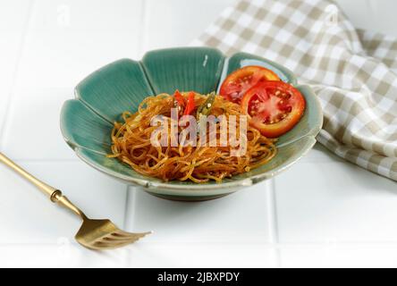 Soun Kecap Pedas oder Fritreis Vermicelli Gebratene Nudelgläser mit süßer Sojasoße, Gewürzen und Chili. Serviert auf Green Bowl, White Table Stockfoto