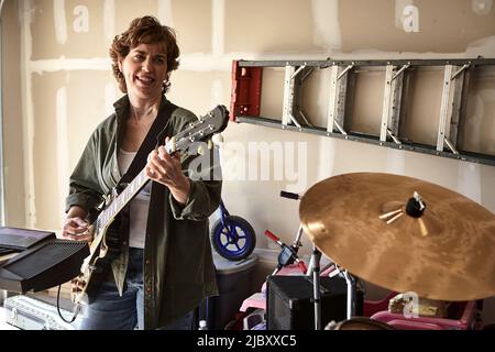 Portrait eines Gitarristen in der Garagenband, bestehend aus Frauen mittleren Alters, die in einer Garage üben Stockfoto