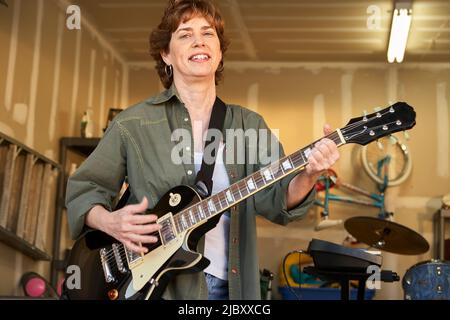 Portrait eines Gitarristen in einer Band, bestehend aus Frauen mittleren Alters, die in einer Wohngarage üben Stockfoto