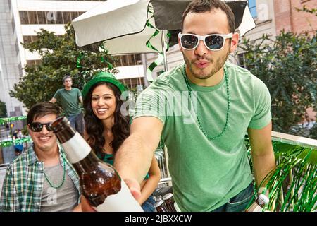 Fröhlicher Mann, der Freunde mit grünen Hüten anstößt und den St. Patrick's Day feiert. Stockfoto