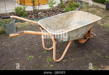 Gartenreinigungsgeräte. Ein leerer Gartenwagen in Nahaufnahme zum Transport von Gülle, Erde und Gras im Garten. Landwirtschaftliche Arbeit. Stockfoto