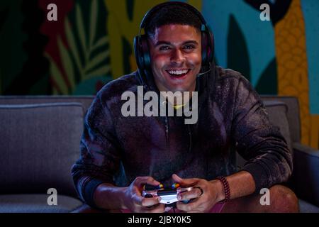 Lächelnder afroamerikanischer Mann spielt Videospiel, während er zu Hause auf dem Sofa sitzt Stockfoto