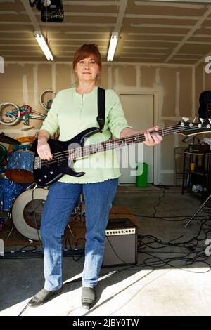 Portrait des Bassisten in der Garage-Band, bestehend aus Frauen mittleren Alters, die in einer Wohngarage üben Stockfoto