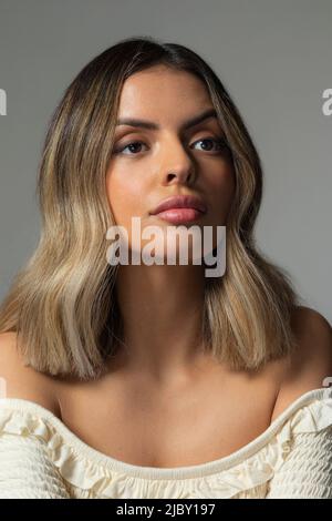 Selbstbewusste junge hispanische Frau, die vor grauem Hintergrund aus der Kamera schaut Stockfoto