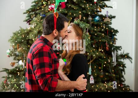 Liebevolles junges Paar, das sich unter dem Weihnachtsbaum küsst. Stockfoto