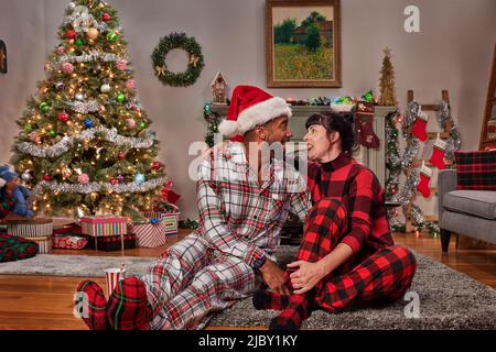 Glückliches Paar, das Weihnachtsmützen trägt und beim Weihnachtsbaum albern ist Stockfoto