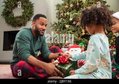 Porträt eines glücklichen afroamerikanischen Vaters und einer Tochter, die gemeinsam Weihnachtsgeschenke eröffnen und lächeln. Stockfoto