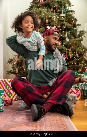 Fröhliche Familie mit Weihnachtsgeschenken, die vor einem beleuchteten Baum sitzen. Stockfoto