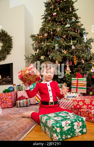 Junge in saisonalen Schlafanzug sitzend an Weihnachtsbaum Eröffnung Geschenke gekleidet. Stockfoto