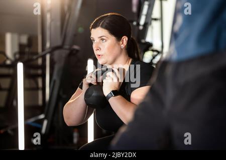 Frau, die im Fitnessstudio arbeitet und Hantel hockt Stockfoto