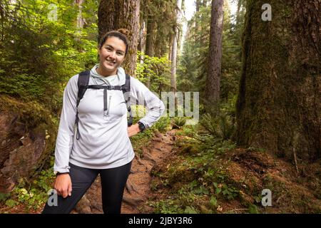Porträt einer jungen kaukasischen Frau, die im Hoh Rain Forest National Park auf der Olympic Peninsula im Bundesstaat Washington auf einem Wanderweg steht Stockfoto