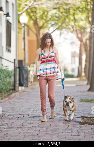 Eine Frau, die mit ihrem englischen Bullenhund eine Straße entlang geht. Stockfoto