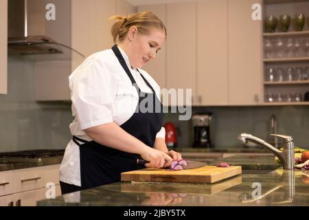 Professioneller Koch Megan Gill in der heimischen Küche schneidet einen Rettich auf Schneidebrett Stockfoto