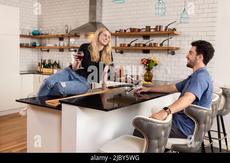 Junge kaukasische Männer und Frauen, die ein Glas Wein trinken, während sie in der Küche sprechen Stockfoto
