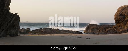 Blick zwischen großen Felsen mit Wellen - Skyline von Surfers Paradise am Horizont Stockfoto