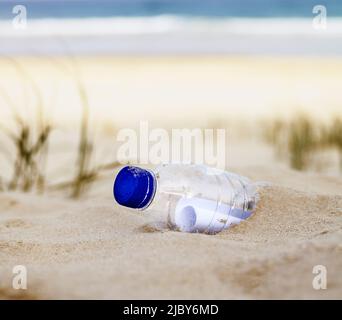 Nahaufnahme der Plastikflasche mit der Nachricht darin halb im Sand vergraben Stockfoto