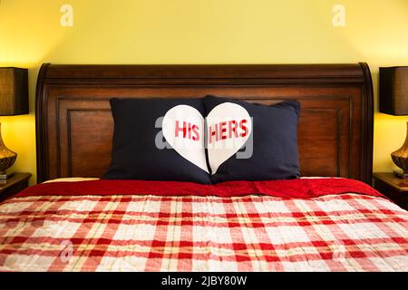 Detailaufnahme von dekorativen Kissen für sie und ihn auf einem dunklen Schlittenbett aus Holz mit rot-weißer karierter Decke im Hauptschlafzimmer des Hauses Stockfoto