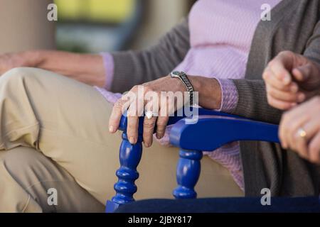 Ein älteres Paar sitzt in Schaukelstühlen, Detail auf der Hand der Frau mit einem Ring auf dem Stuhl Stockfoto