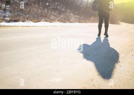 Frau im Winter warme Jacke auf der Straße bei Sonnenuntergang im Winter trägt einen Rucksack auf der Schulter. Stockfoto