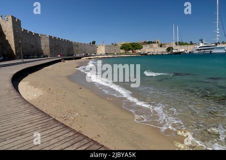 Stadtstrand und Holzsteg. Und Rhodos Burgmauern, Rhodos Insel, Griechenland, Dodekanes. Mai 2022. Feder. Stockfoto