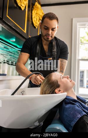 Stylistin, die die Haare einer jungen Frau im Waschbecken des Boutique-Salons wäscht Stockfoto