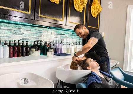 Stylistin, die die Haare einer jungen Frau im Waschbecken des Boutique-Salons wäscht Stockfoto