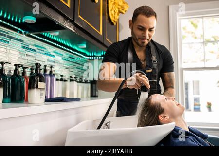 Stylistin, die die Haare einer jungen Frau im Waschbecken des Boutique-Salons wäscht Stockfoto