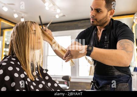 Stylistin schneidet im Boutique-Salon die Haare einer jungen Frau in einem gepunkteten Cape Stockfoto