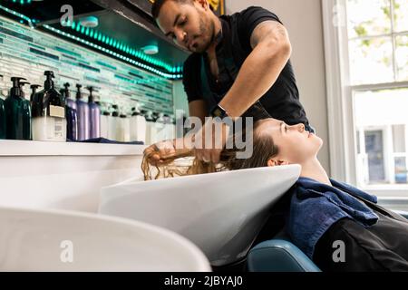 Stylistin, die die Haare einer jungen Frau im Waschbecken des Boutique-Salons wäscht Stockfoto