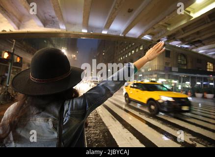 Schöne, modische junge Frau, die in einer regnerischen, stürmischen Nacht in Manhattan, New York City, NY, ein Taxi in der 42. Street vor der Grand Central Station anhagelt Stockfoto