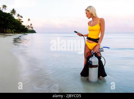 Junge Frau, die am tropischen Strand steht und ihre Tauchausrüstung überprüft Stockfoto