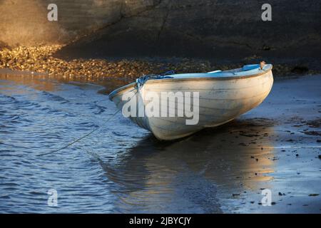 Beiboot am Ufer des Sandstrandes vor einer felsigen Klippe gebunden Stockfoto