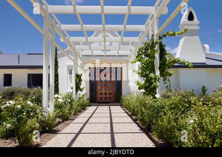 Weiße Pergola und weiße Rosen führen zum Vordereingang des Gehöfts im holländischen Stil im Weingut Stockfoto