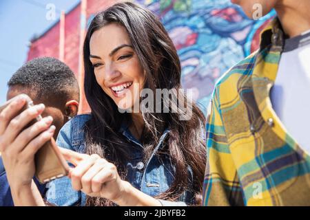 Eine Gruppe junger Mitarbeiter, die mit dem Mobiltelefon vor einer graffidiert Wand hängen Stockfoto