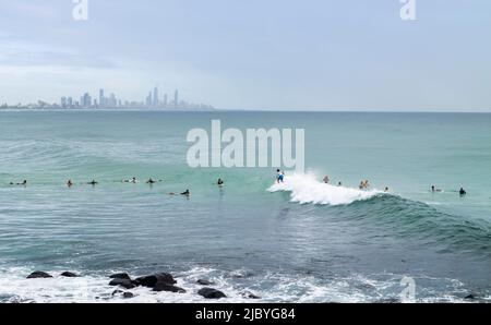 Surfer im Wasser an der Küste von Burleigh Heads und Surfers Paradise am Horizont Stockfoto