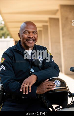 Porträt eines Polizisten, der draußen auf seinem Motorrad sitzt und lächelnd auf die Kamera blickt Stockfoto