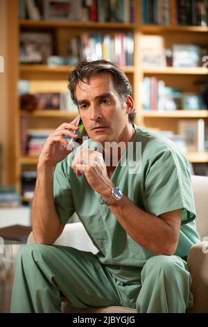 Hispanischer Arzt, der in seinem Büro Telemedizin praktiziert und mit dem Patienten am Handy spricht Stockfoto