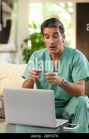 Hispanischer Arzt, der von zu Hause aus Telemedizin praktiziert, mit einem Laptop-Computer, um den Patienten bei einem Videoanruf zu konsultieren Stockfoto